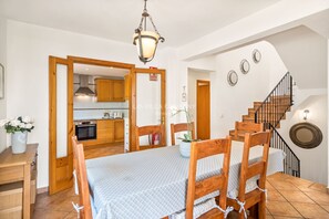 A dining area with a wooden table and chairs, a hanging light fixture, and a staircase with a railing. - Fabulous Villa with Private Pool in Tranquil Area, Sleeps 8 (Cala Molí)