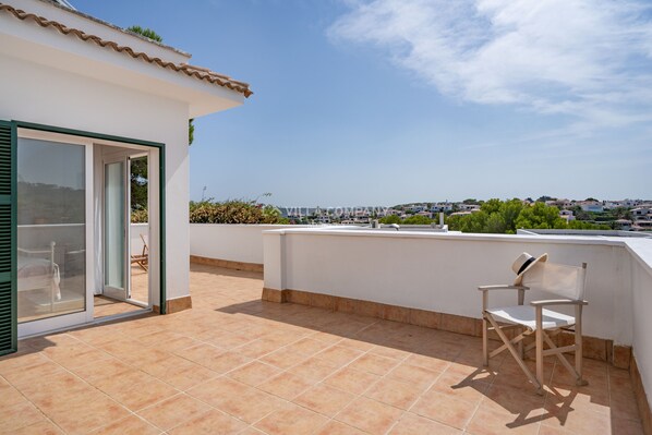 A balcony with a chair, a sliding glass door, and a view of a town. - Fabulous Villa with Private Pool in Tranquil Area, Sleeps 8 (Cala Molí)