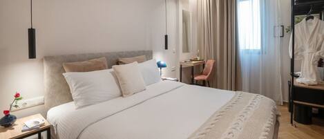 A modern hotel room with a large bed, a desk, a chair, and a robe rack.