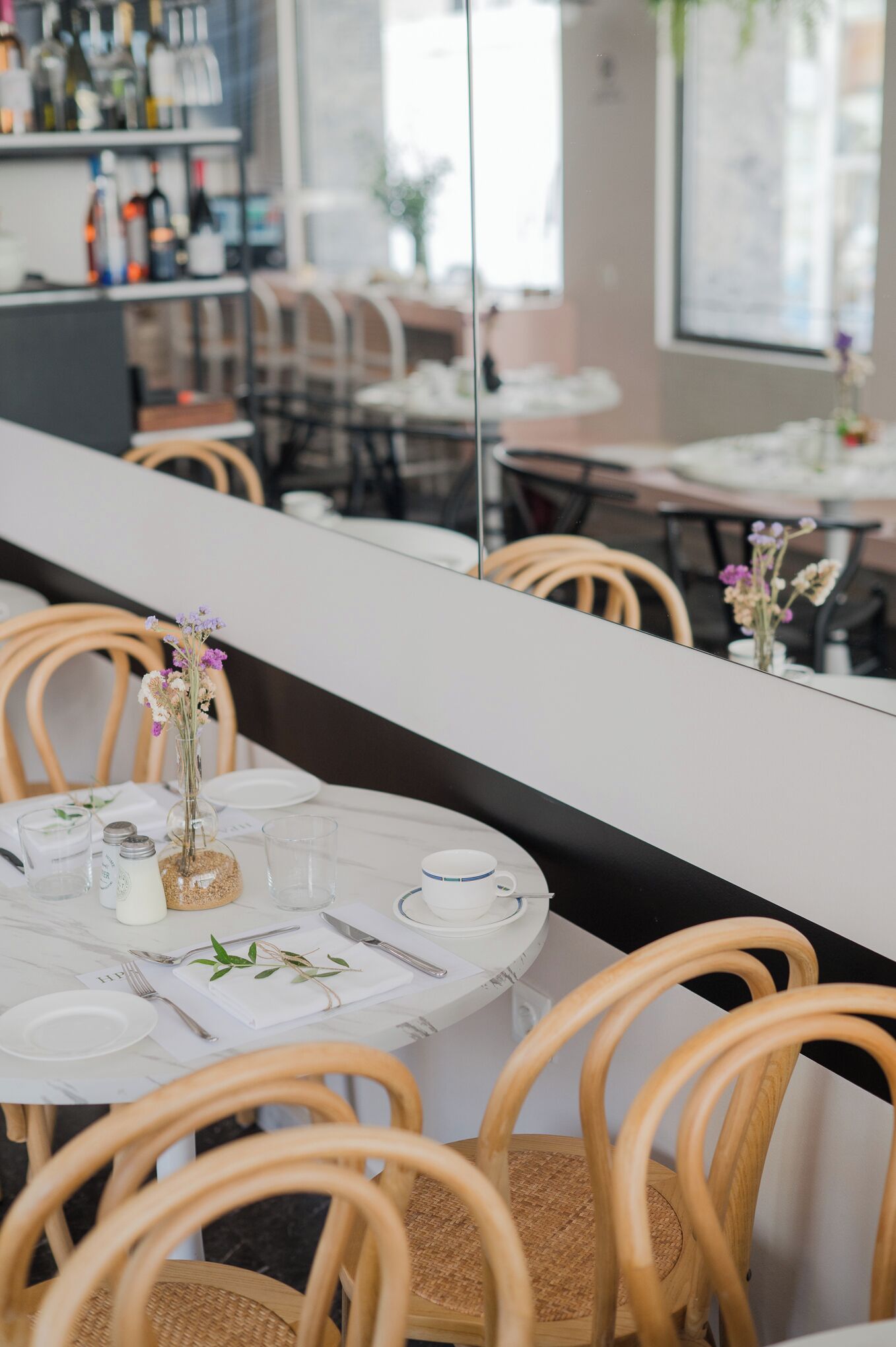 Un interior de restaurante con mesas redondas, sillas de madera y una encimera de mármol blanco.