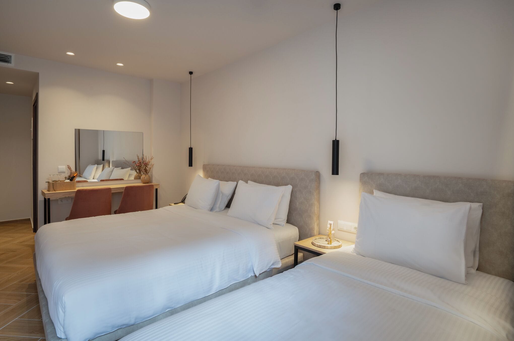 Hotellihuone, jossa on kaksi sänkyä, työpöytä, tuoli, peili ja yöpöytä, jossa on lamppu.