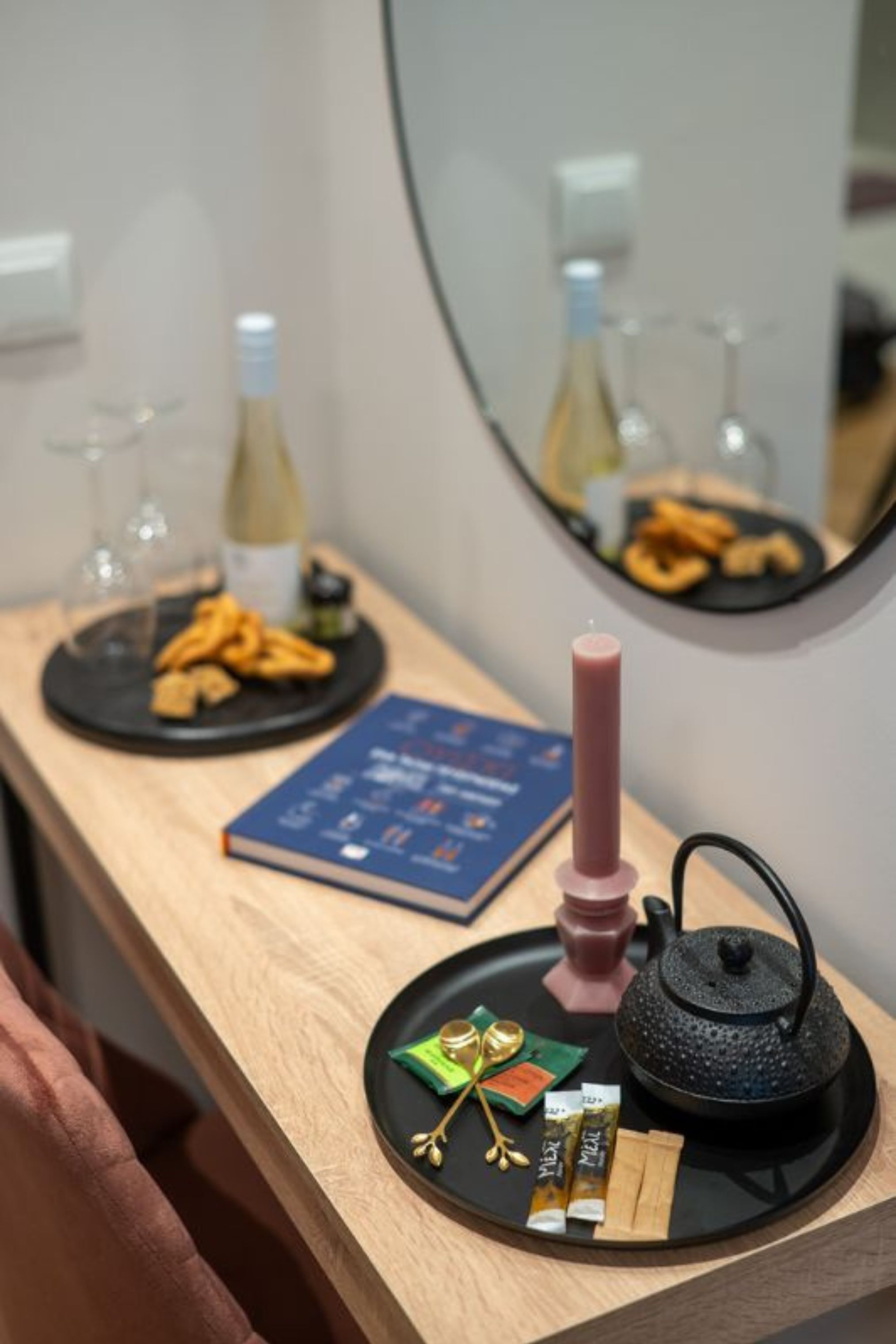 Une table en bois sur laquelle se trouvent un livre, une bougie, une théière et divers aliments.