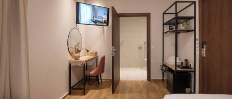 A hotel room with two beds, a desk with a chair, a TV mounted on the wall, a shower area, and a wooden wardrobe.