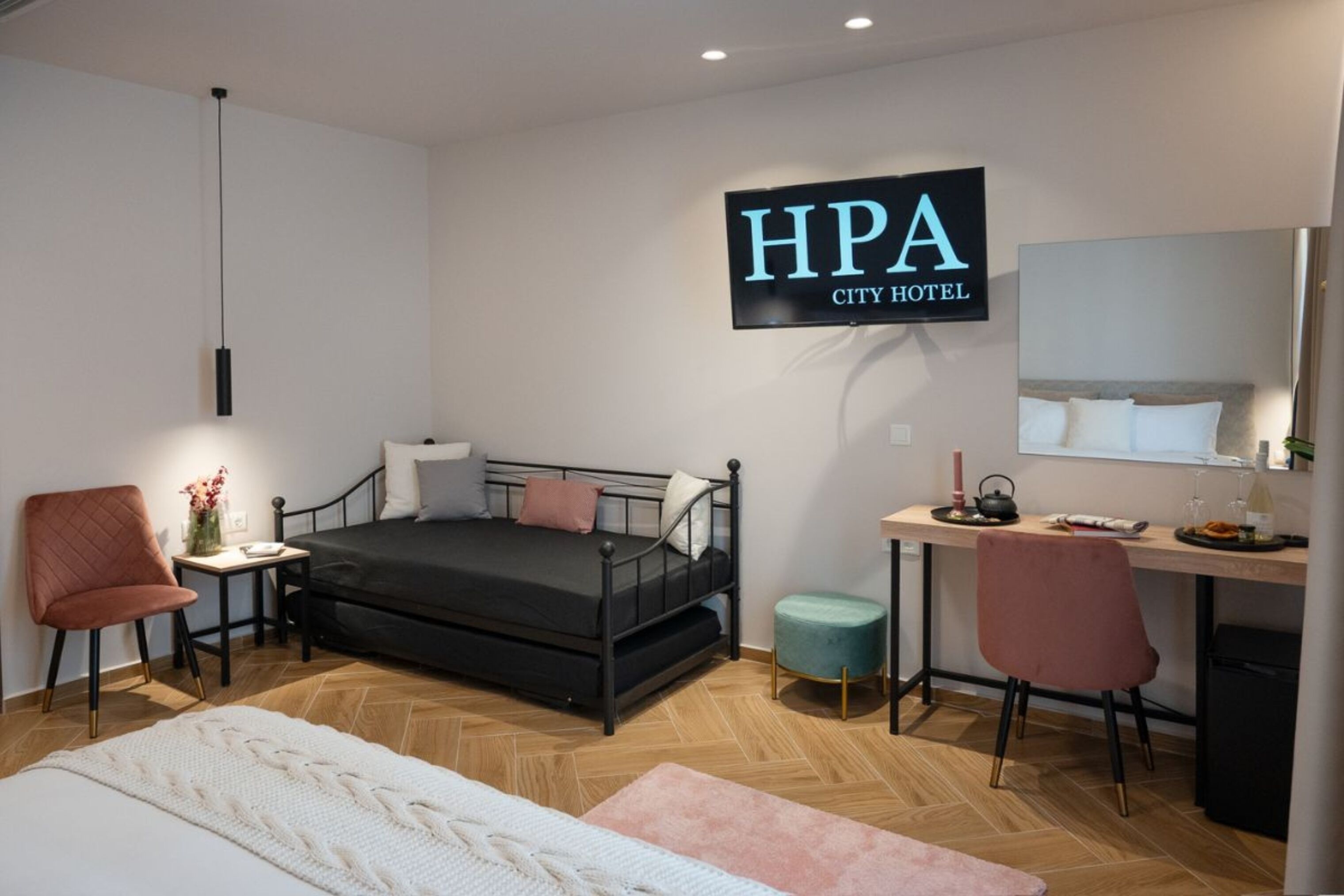 A modern hotel room with a bed, a desk, a chair, and a TV displaying "HPA City Hotel".