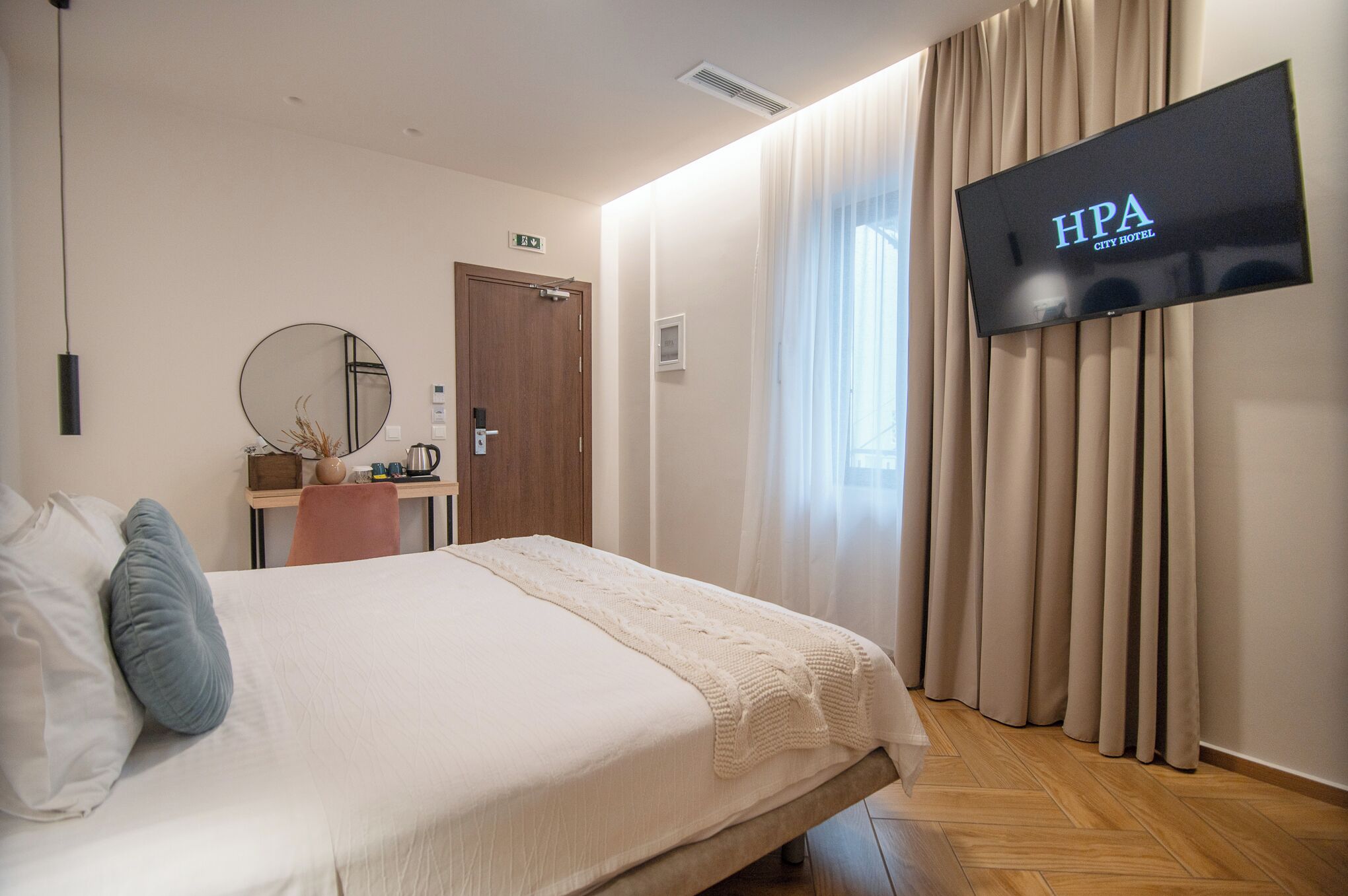 A hotel room with a bed, a TV mounted on the wall, a wooden desk, and a mirror.