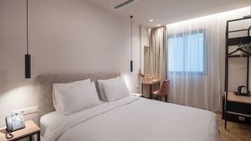 A hotel room with a large bed, bedside table with a phone, a desk with a chair, and a mirror.