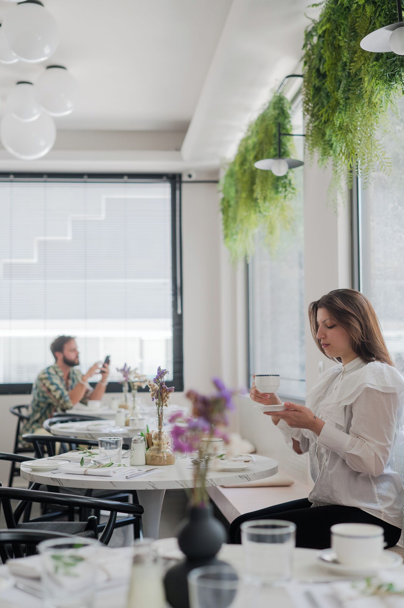 A dining area with round tables, white tablecloths, and hanging plants.