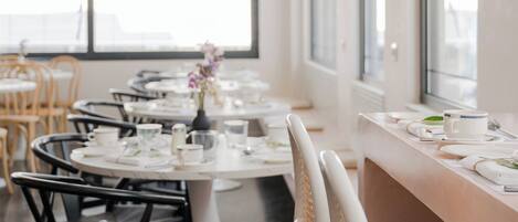 A modern dining area with round tables, black and white chairs, and hanging greenery.