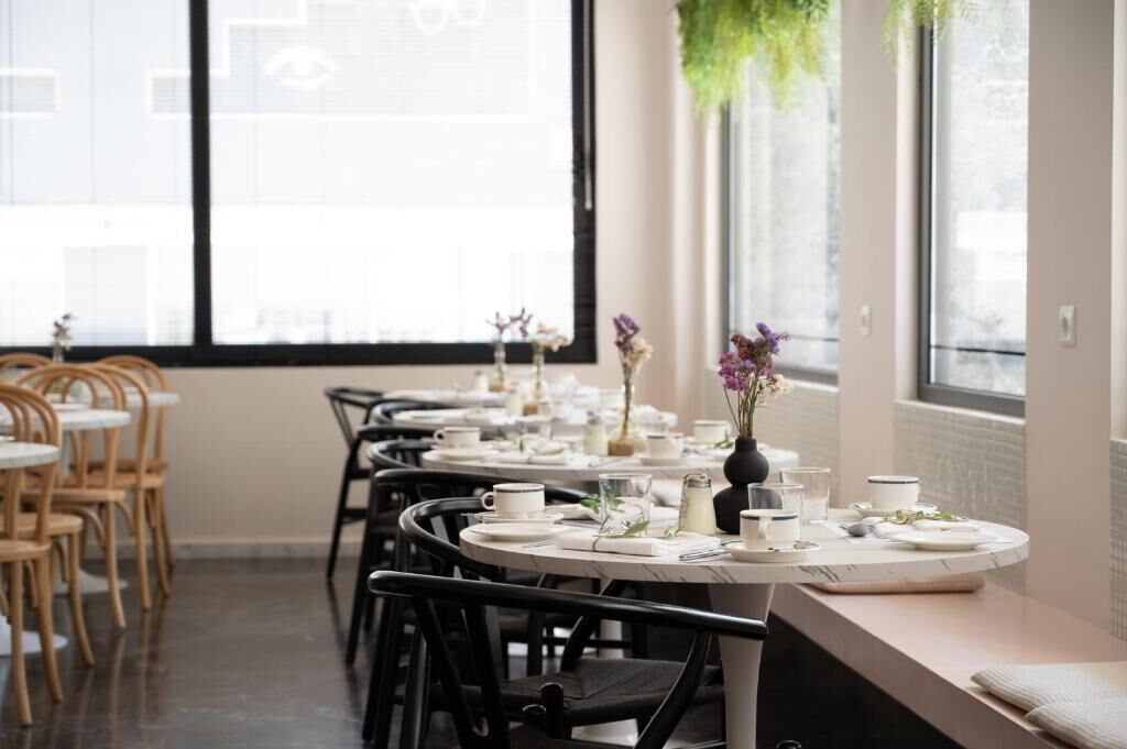 A dining area with round tables set for two, equipped with white tablecloths, plates, and cutlery.