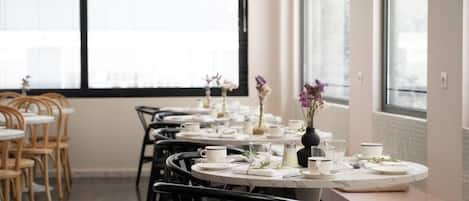 A dining area with round tables set for two, equipped with white tablecloths, plates, and cutlery.