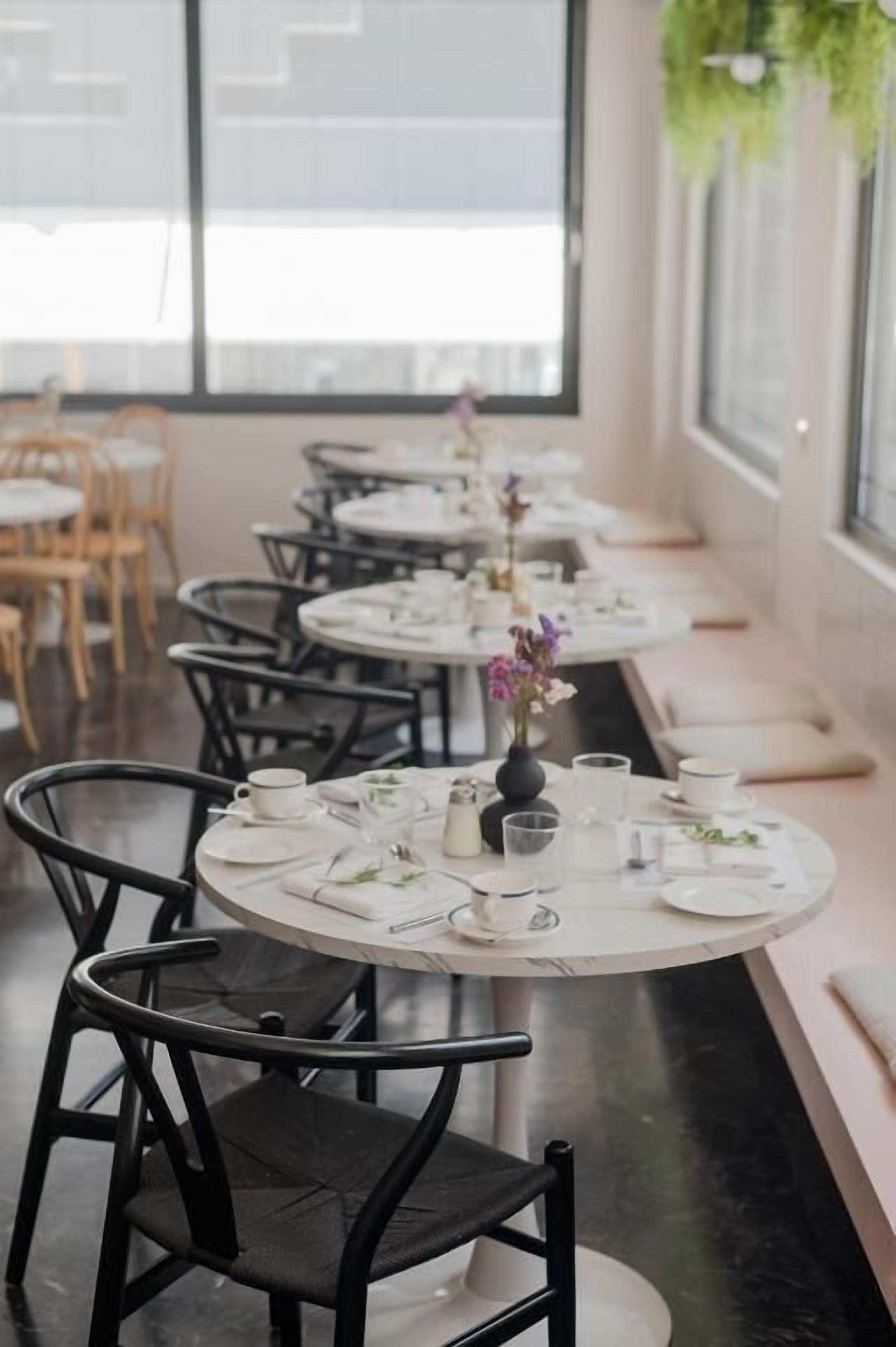 A restaurant with round tables set with white tablecloths, black chairs, and small centerpieces.