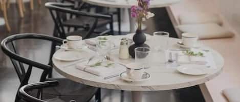 A restaurant with round tables set with white tablecloths, black chairs, and small centerpieces.