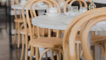 Ein Restaurantinneres mit runden Tischen und Holzsesseln, einem Tisch aus weißem Marmor und einer Theke mit verschiedenen Flaschen und Gläsern.