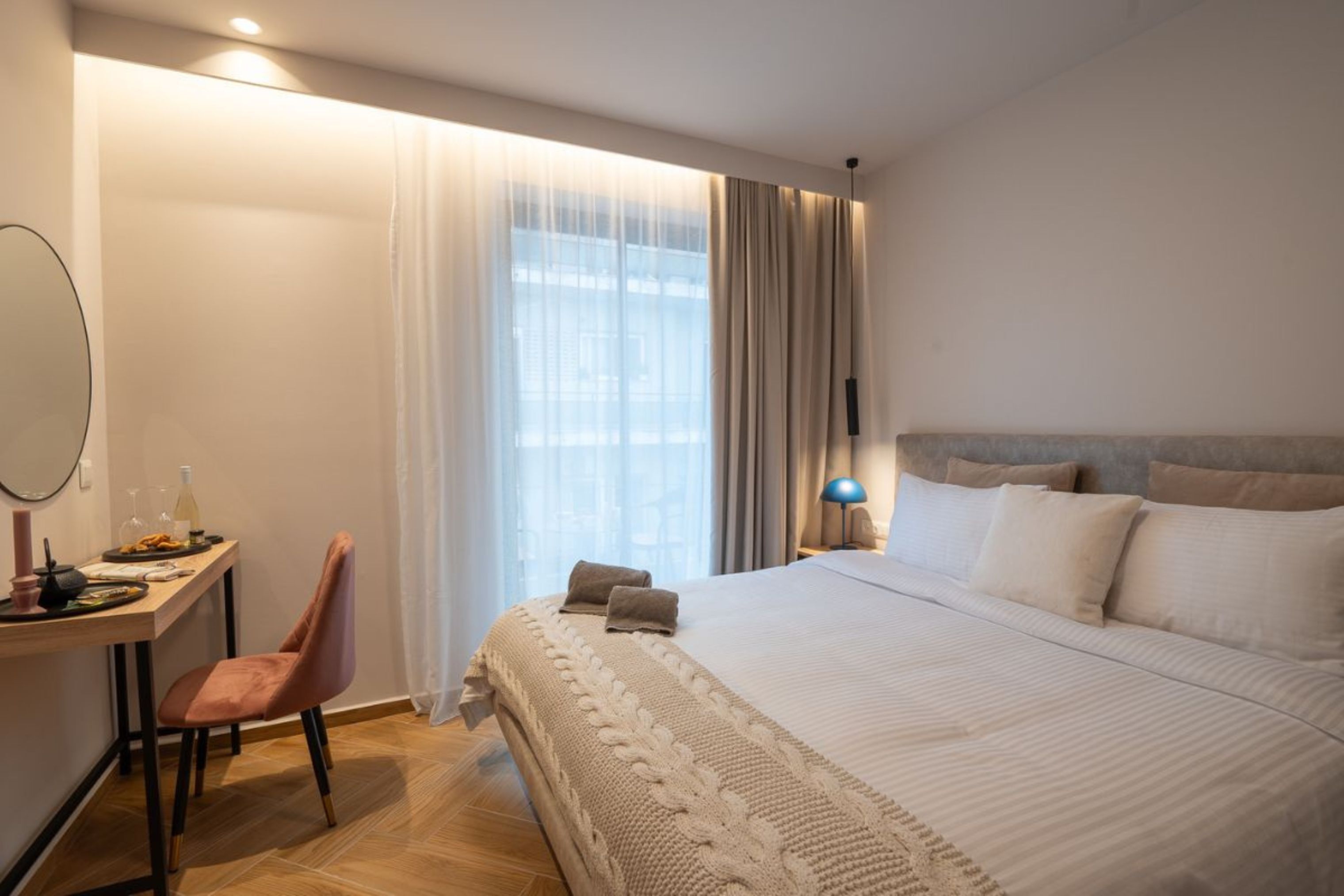 Una habitación de hotel con una cama, un escritorio con silla, una lámpara y un ventanal con cortinas.