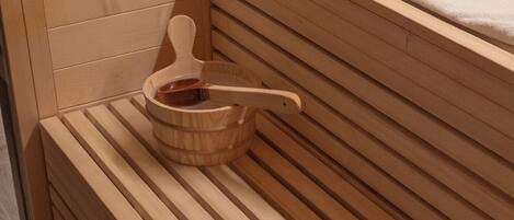 A wooden sauna with a bench, a wooden bucket with a ladle, and a towel on the bench.