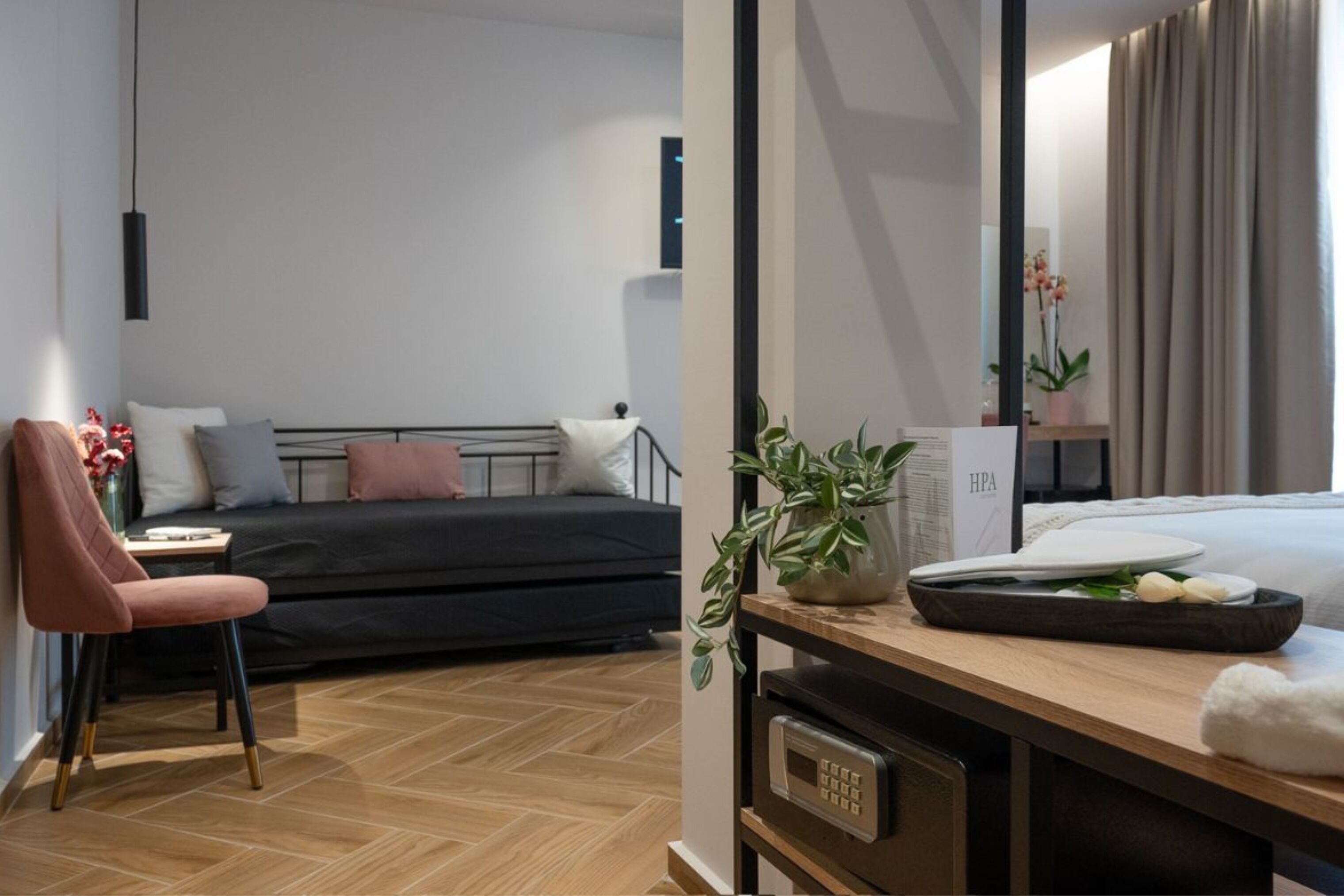 A modern hotel room with a bed, a desk with a computer, a chair, and a potted plant.