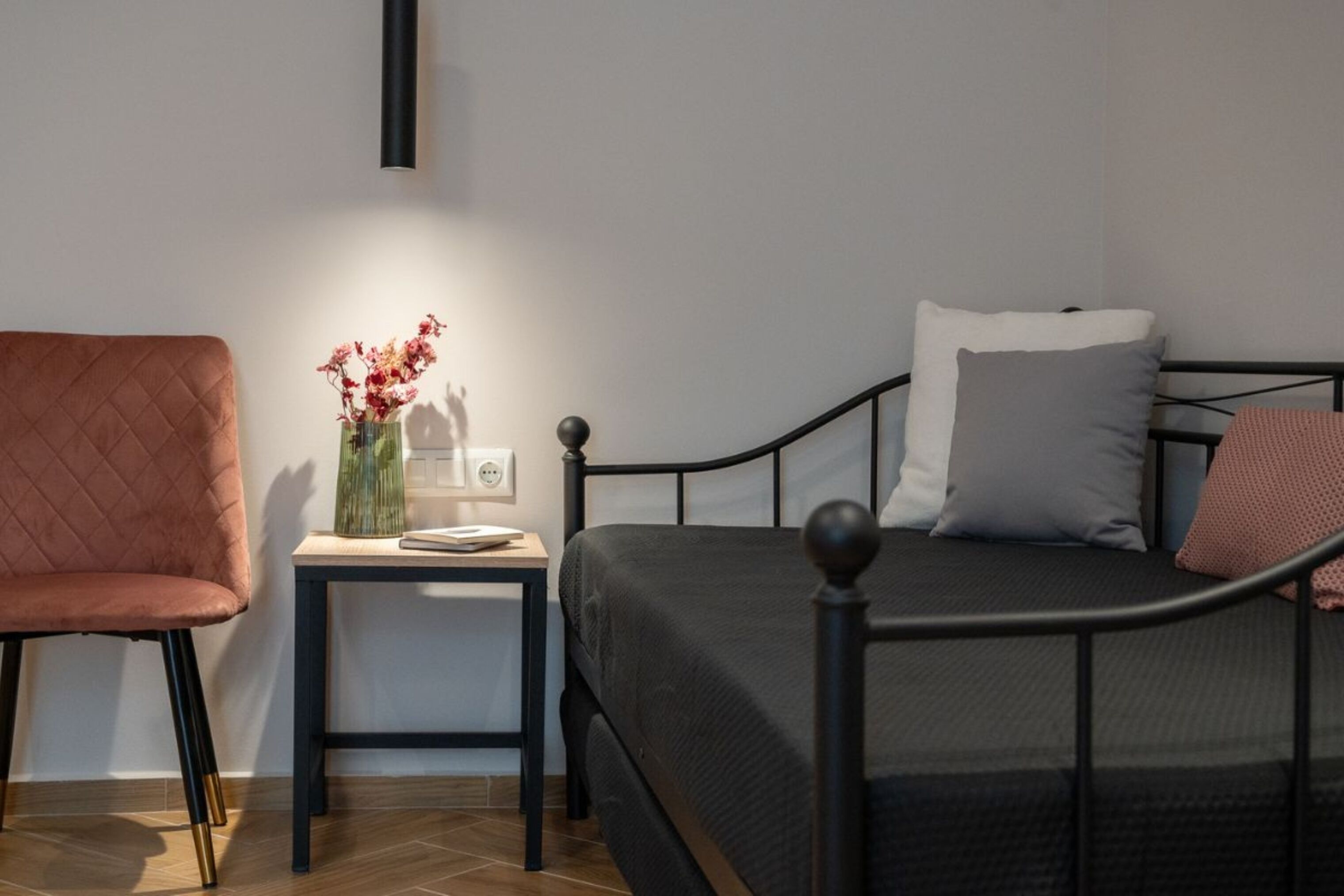 A neatly arranged bedroom with a bed, a side table, a chair, and a vase with flowers.