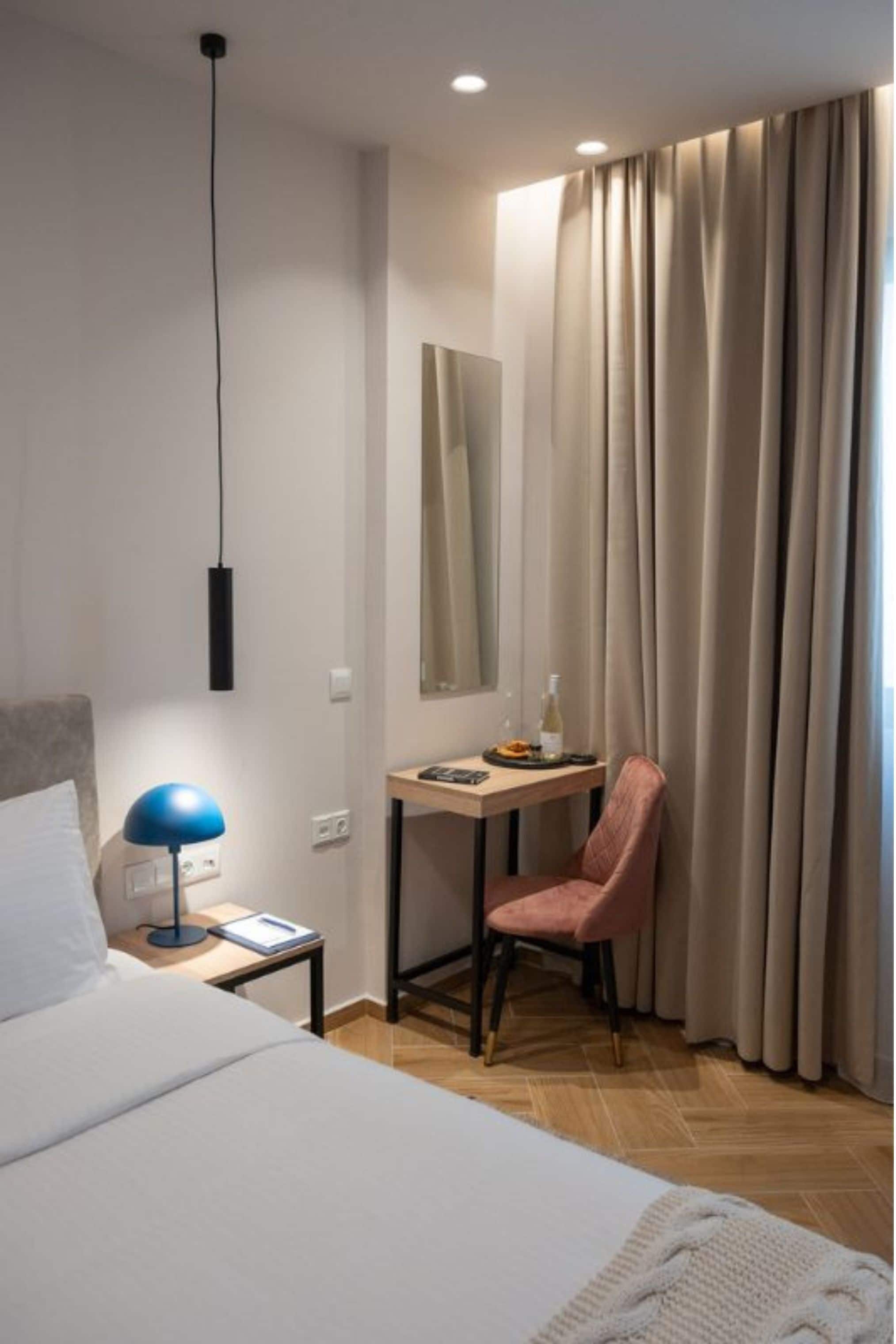 Habitación de hotel con cama, escritorio, silla, lámpara y ventana con cortinas.