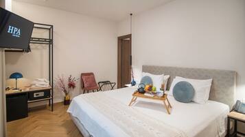 A hotel room with a bed, a TV, a desk, a chair, and a tray with fruits and a vase.