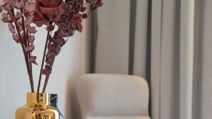 A modern hotel room with a comfortable armchair, a small side table with a vase of flowers, a bottle, and a glass. - IRA-HPA Hotel (Kalamata)