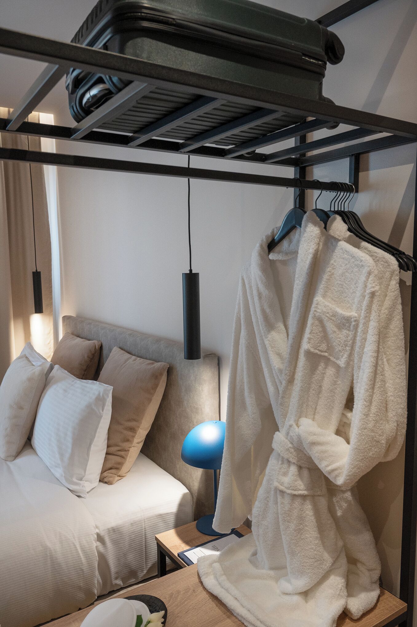 A hotel room with a bed, a bedside table, a lamp, a robe hanging on a rack, and a ceiling fan.