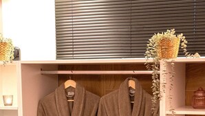 A bathroom with two hanging robes, a wooden cabinet, and a shelf with toiletries. - IRA-HPA Hotel (Kalamata)
