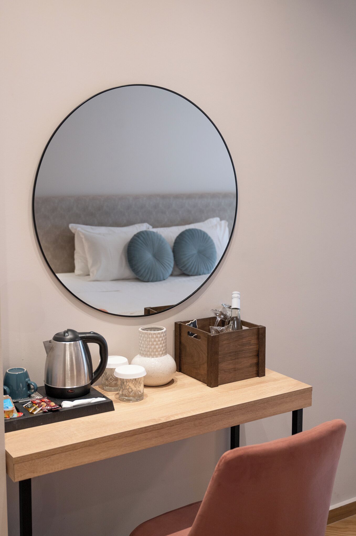 Una habitación moderna con un espejo redondo, un escritorio de madera, una silla rosa y una cama con almohadas azules.
