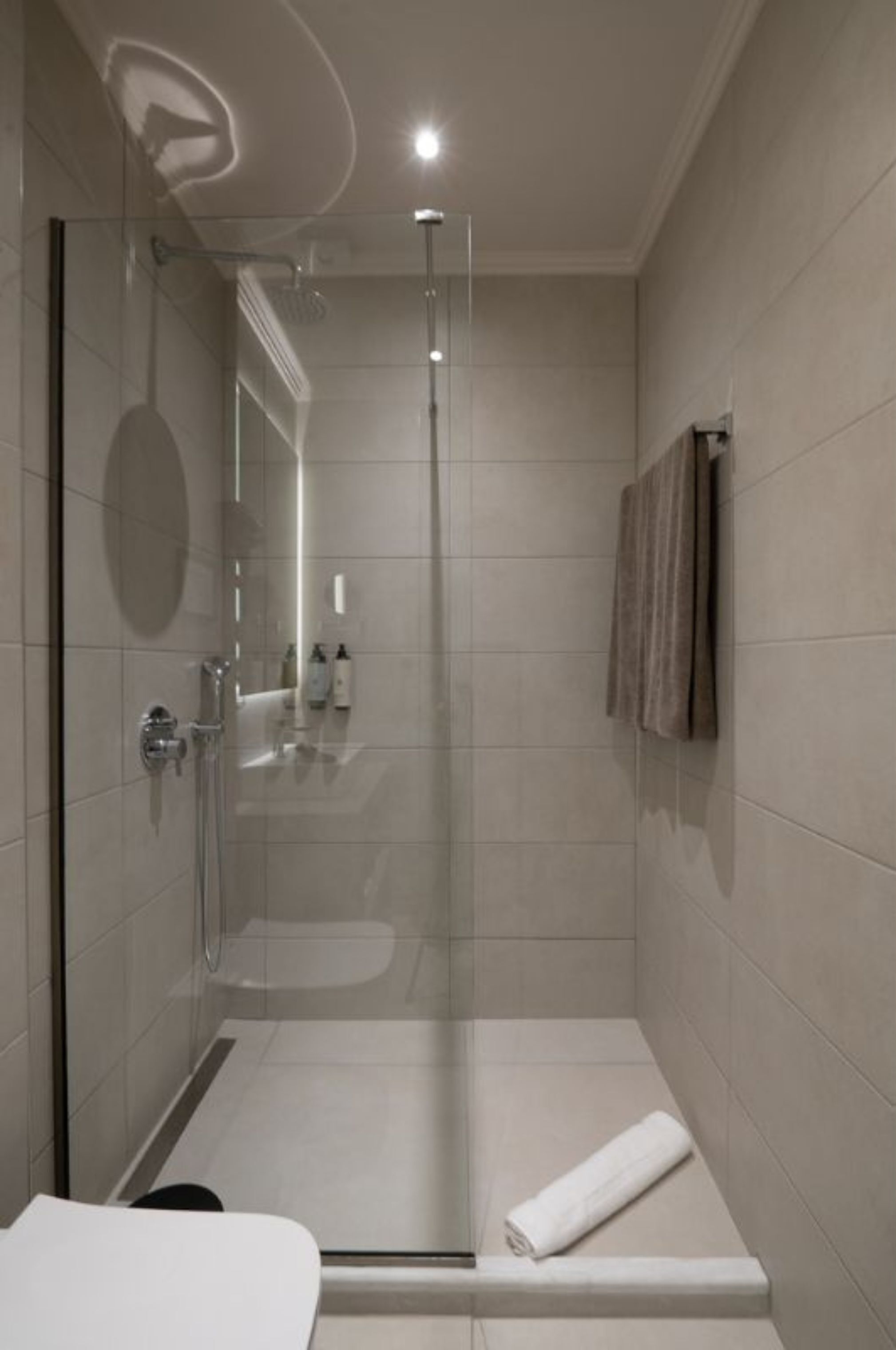 A modern bathroom with a glass-enclosed shower, a white sink, and a towel rack.
