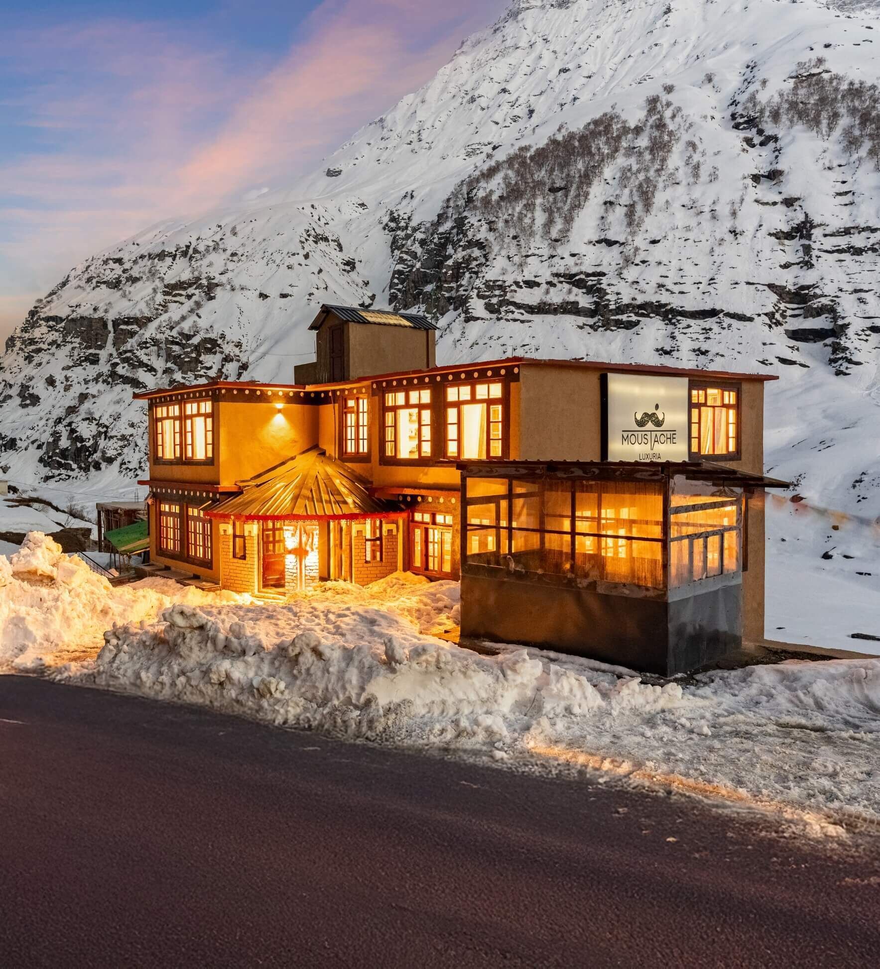 A two-story building with a sign reading "Mousache Luxury" in a snowy mountainous area.