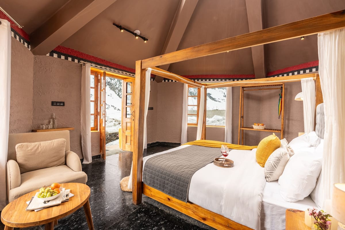 A spacious bedroom with a four-poster bed, a sitting area with a table, and a view of the outdoors.