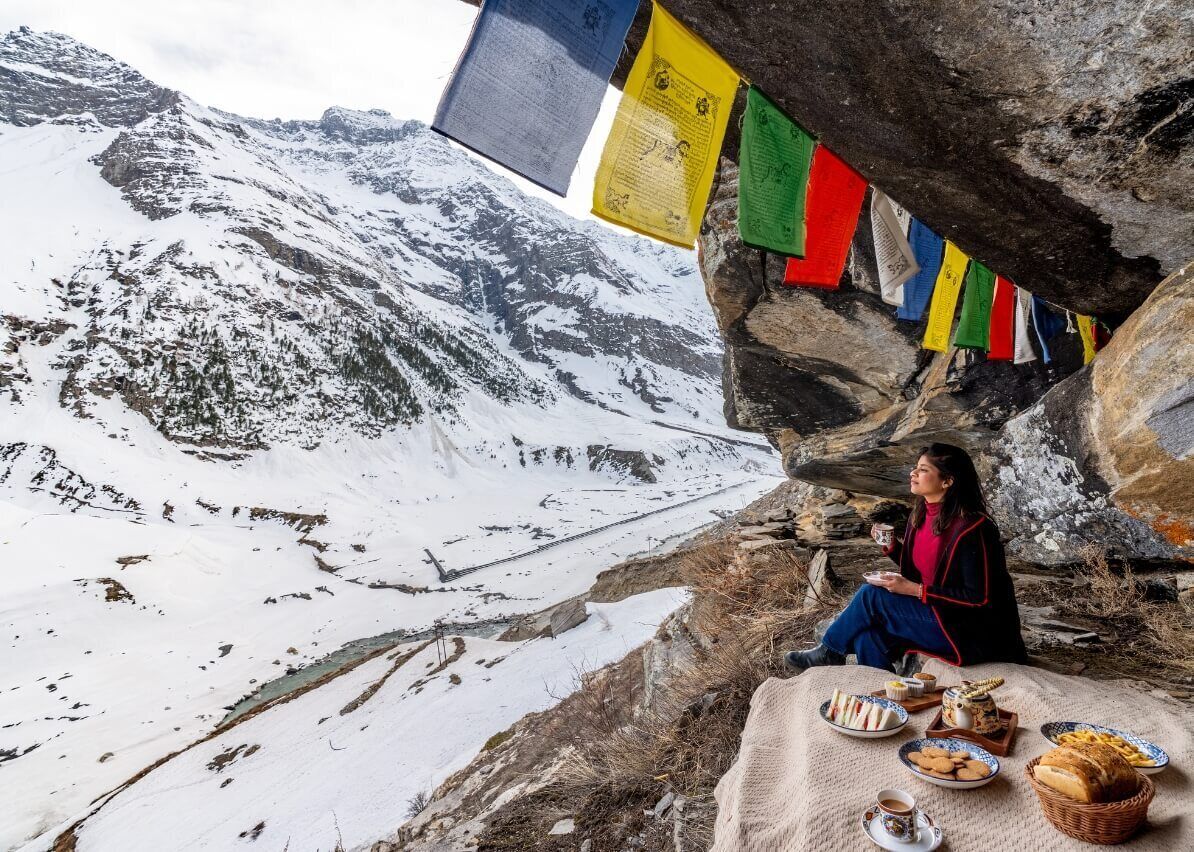 A person sitting on a rock with a table of food and prayer flags in the background.