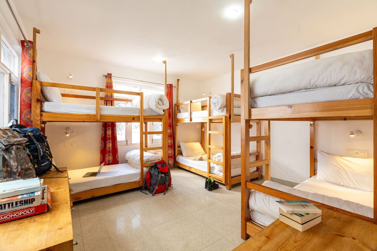 A dormitory with bunk beds, a wooden desk, and a window with curtains.