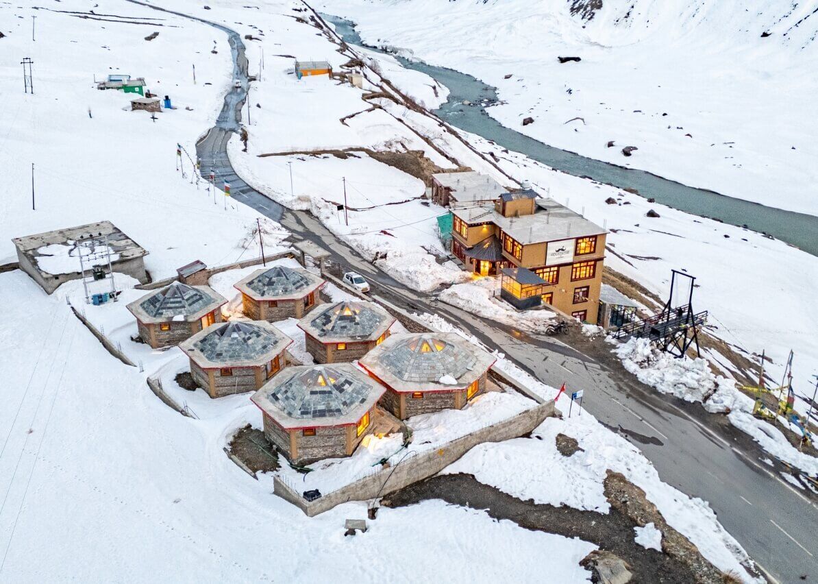 A snow-covered village with several stone buildings, a main lodge with a large balcony, and a winding road.