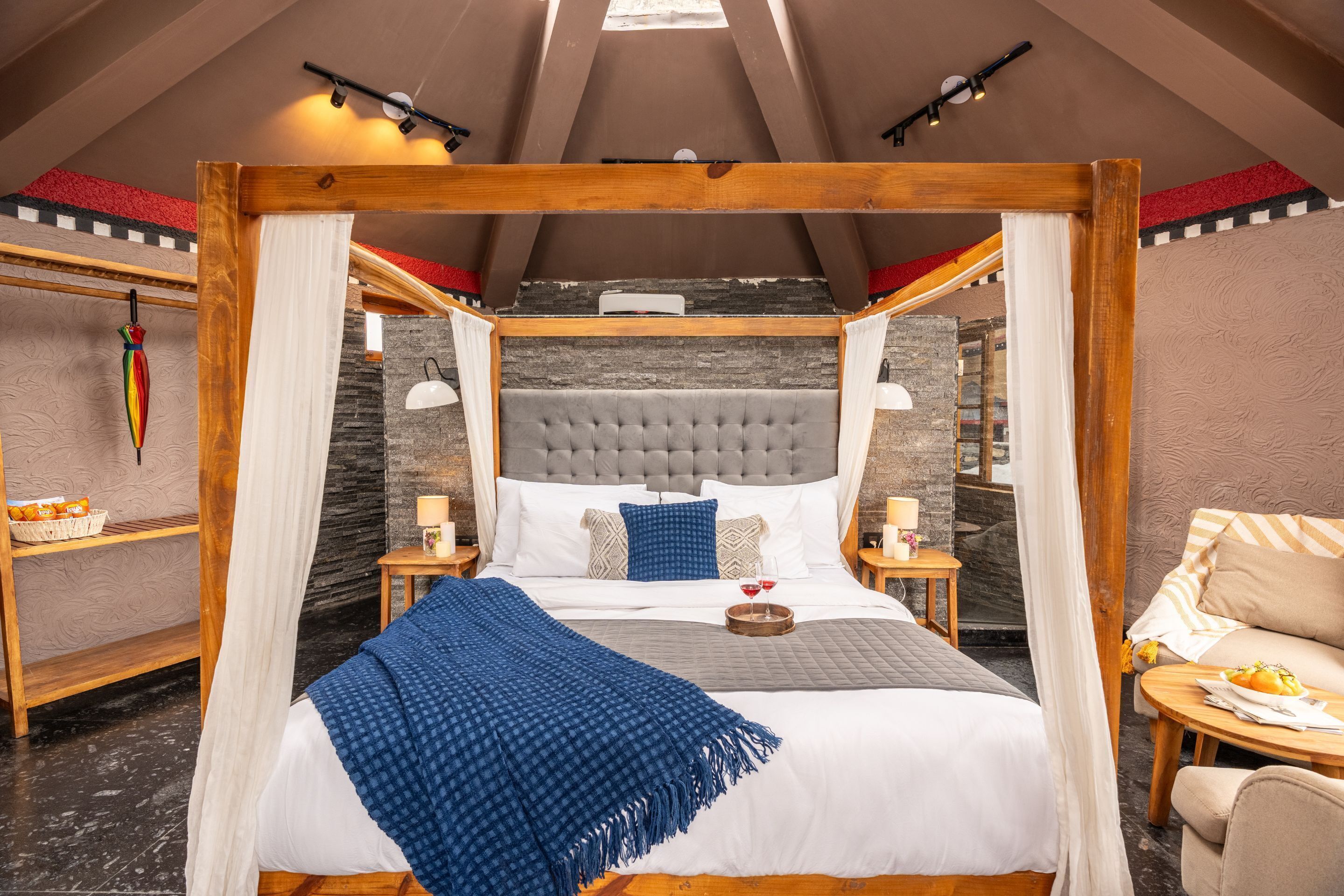 A spacious bedroom with a large bed, wooden canopy, and a stone wall backdrop.