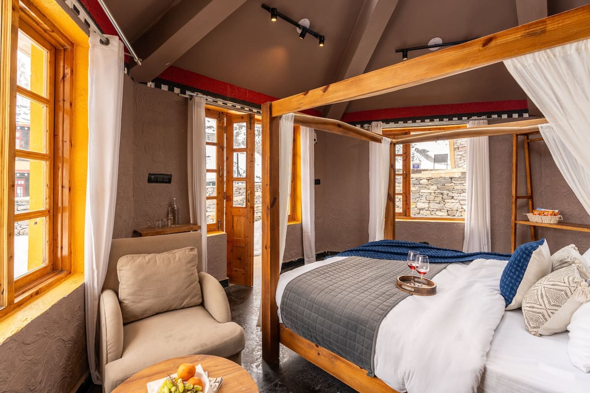 A bedroom with a four-poster bed, a sofa, a small table with fruit, and a view of the outside.