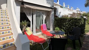 En patio med et bord og stole, et overdækket siddeområde og en trappe med dekorative fliser.