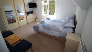 Une chambre à coucher avec un lit, une télévision, une fenêtre, une commode et un bureau.