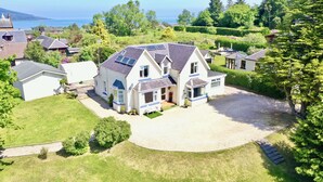 Une grande maison à deux étages dotée d’un patio couvert, de panneaux solaires et d’une pelouse bien entretenue.