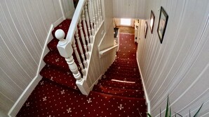 Un escalier recouvert d’une moquette rouge, avec des murs blancs, menant à une pièce dotée d’une fenêtre et d’un tableau encadré accroché au mur.