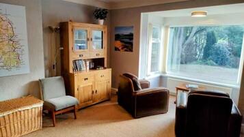 A cozy living room with a wooden cabinet, a sofa, a chair, and a large window with a view of trees.