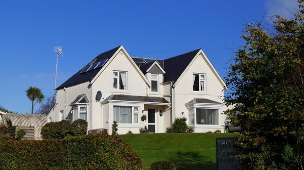 A two-story house with a sloped roof, multiple windows, and a well-maintained lawn. - Allandale House (Isle of Arran)