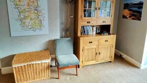 Une pièce avec une carte accrochée au mur, un meuble en bois rempli de livres, une chaise et un panier en osier.
