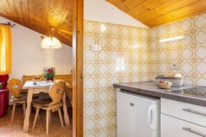 Techo de madera, una mesa de comedor con sillas, una zona de cocina con refrigerador y azulejos con diseño.