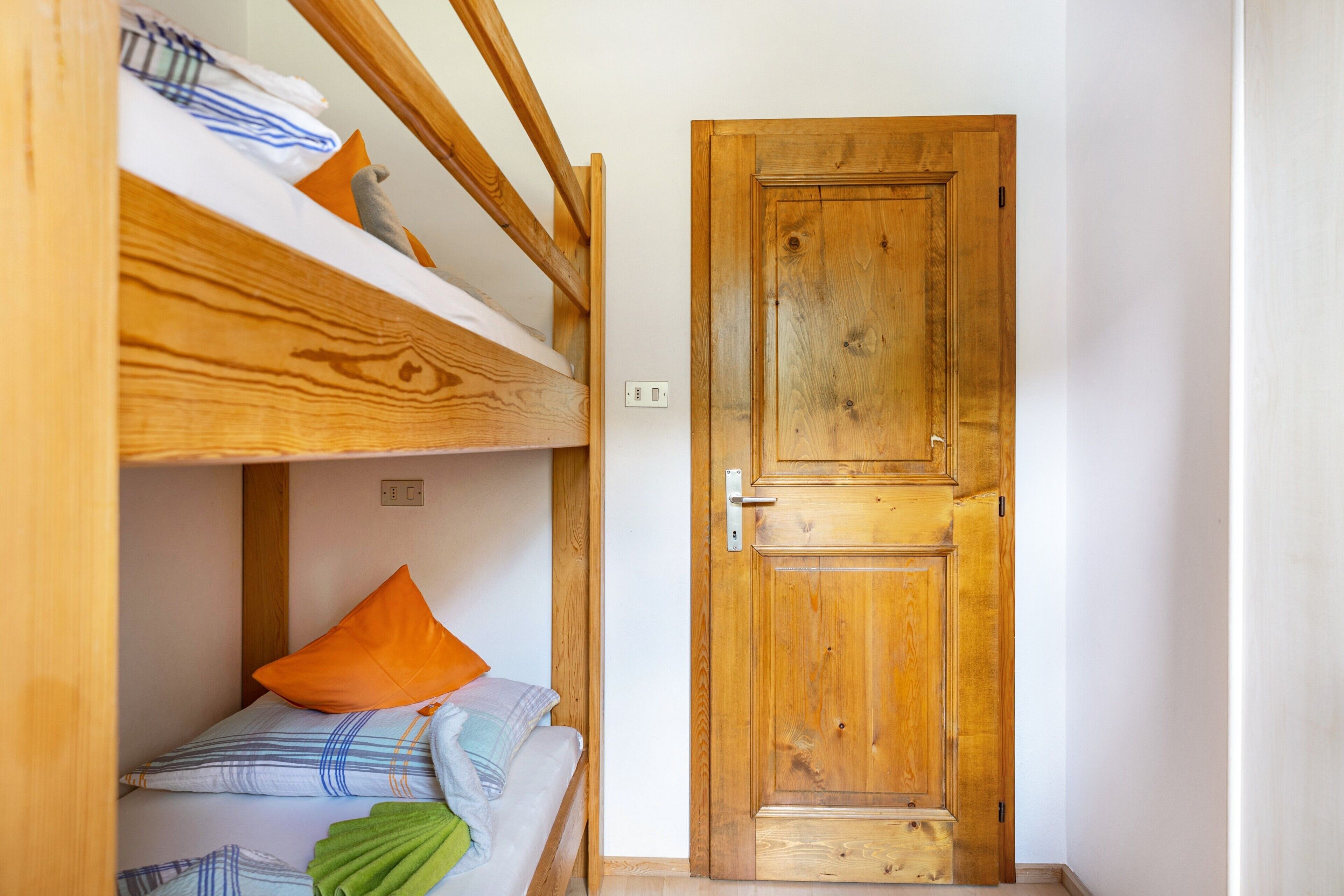 Una habitación con literas, una puerta de madera y un interruptor de luz en la pared.