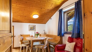 Techo de madera, una mesa de comedor con sillas, un sofá de cuero rojo y una ventana con cortinas.
