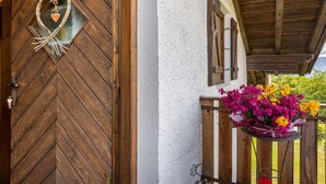 Una puerta de madera con un espejo en forma de corazón, un balcón con un arreglo floral y una pared blanca con textura.
