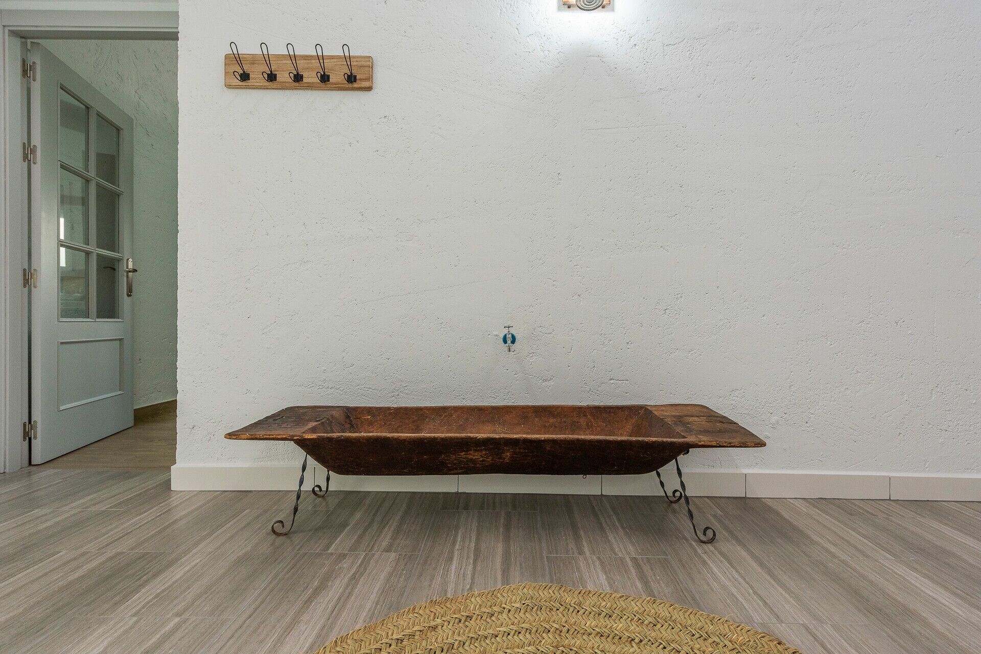 A room with a wooden bench, a wall-mounted coat rack, and a door.