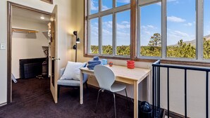 Una habitación con escritorio, silla y un amplio ventanal que ofrece vistas a árboles y colinas.