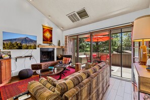Una sala de estar con chimenea, un sofá grande, una mesa de comedor y vistas al exterior a través de un ventanal corredero.