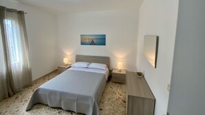 A bedroom with a bed, two bedside tables with lamps, a painting on the wall, and a mirror.